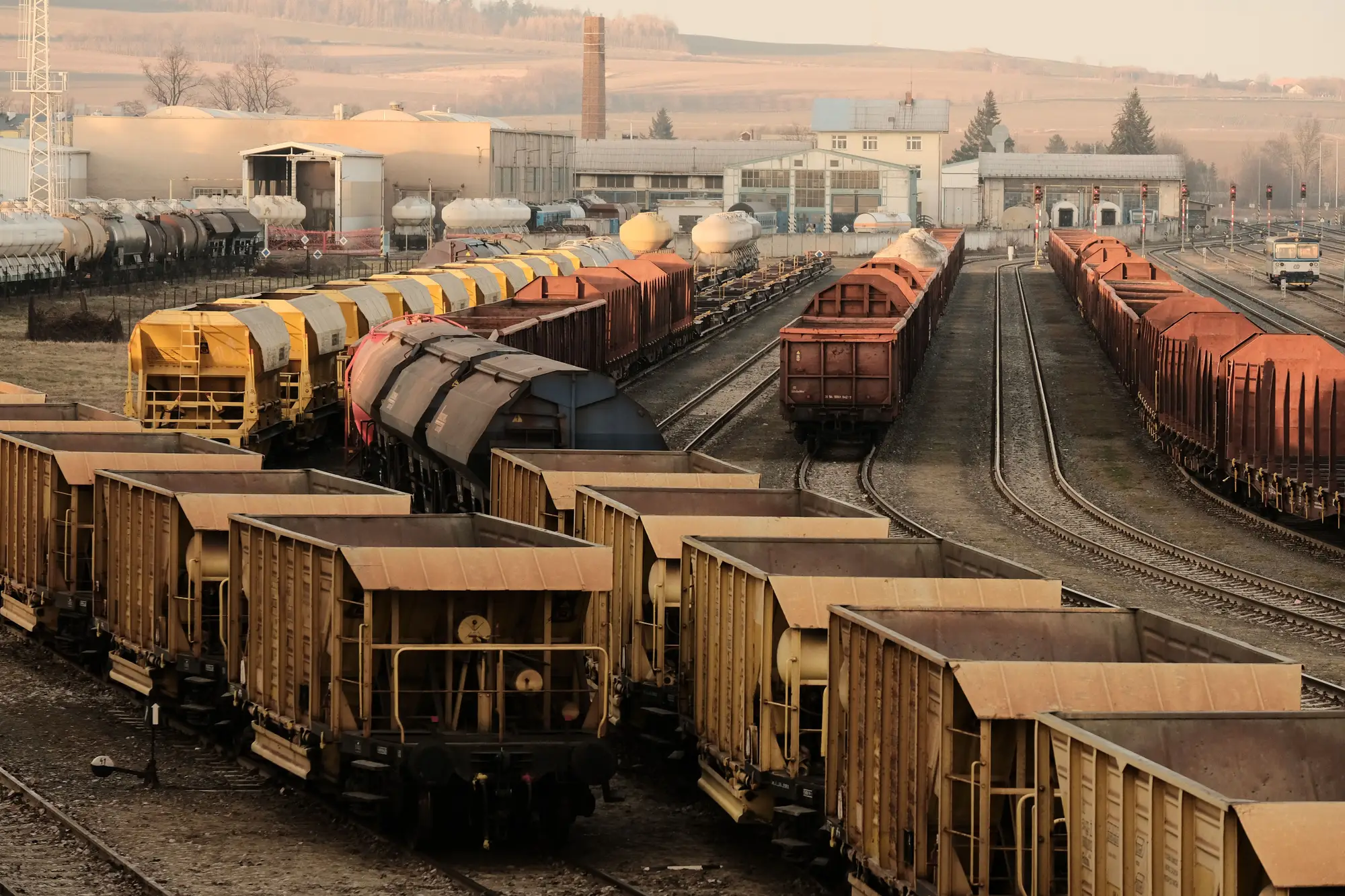 A freight yard in low evening light, with rakes of hopper and covered wagons standing on several sidings
